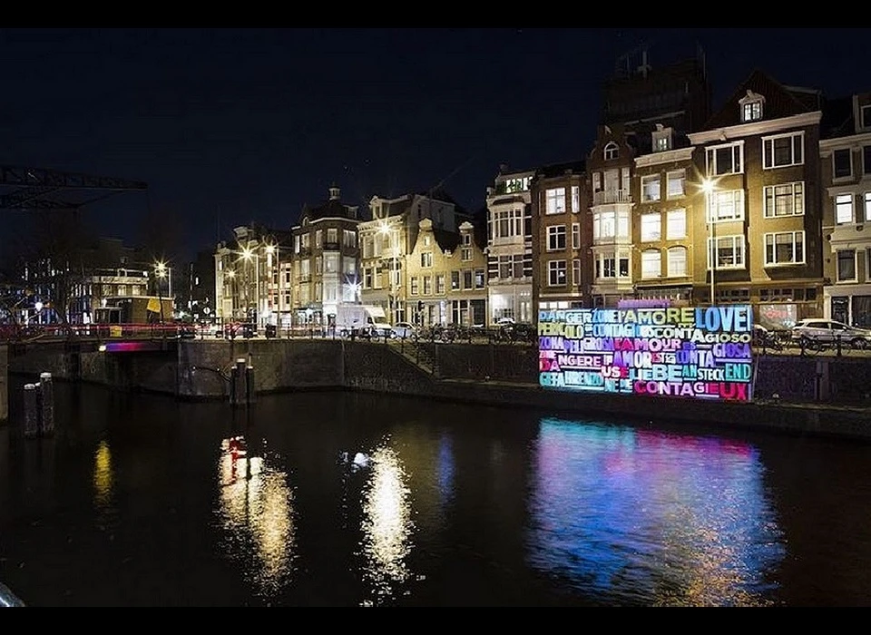 'Together'. Liefde werkt aanstekelijk, dus waarom waarschuwen deze kunstenaars ons dan voor een gevarenzone? Bedoelen ze dat liefde besmettelijk is, 
					  of dat we controle verliezen? Wat betekent liefde nog in dit tijdperk van individualiteit en losse verbanden? Het gebruik van taal heeft altijd een grote rol gespeeld in de lichtkunst. De kunstenaars maken een 
					  statement in verschillende talen, verwijzend naar het internationale karakter van Amsterdam. Bewoners en bezoekers dragen daar op een eigen manier aan bij, in een eigen taal. Maar de enige taal die iedereen spreekt 
					  blijft natuurlijk liefde. (Luigi Console (IT) onderzoekt multimediagebruik, met name de relatie tussen verschillende media zoals posters, video mapping en creative coding. Valentina Novembre (IT) onderzoekt menselijke 
					  relaties, het gebruik van spraak en storytelling en past dat met digitale media toe in sociale projecten.) 2016