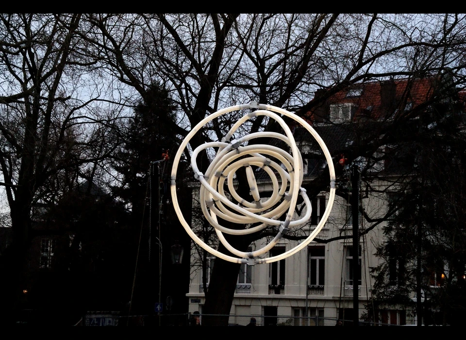 Beweging staat centraal in de 7 meter hoge installatie 
					  van Lambert Kamps. Negen lichtgevende cirkels draaien onophoudelijk in en uit elkaar, de grootste met een diameter van 4 meter, de 
					  kleinste slechts 70 centimeter. De draaiende ringen doen denken aan planetaire ringen zoals je die vindt bij Jupiter of Saturnus 
					  of aan de draaiende elektronen rondom een atoom. 2019