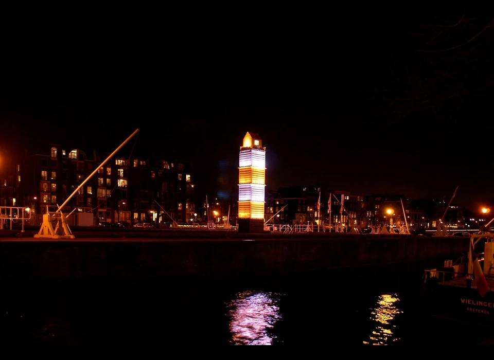 Deze vuurtoren is niet wat het lijkt. Het is een zeecontainer, afkomstig van een schip dat zijn lading verloor. Een wit huisje, omgeven 
					  door een wit houten hekje. Uit het huisje stroomt ’s nachts licht. Het werk is een ode aan Amsterdam, een stad die sterk door de internationale scheepvaart is beïnvloed en gevormd. Tegelijkertijd is 
					  ‘LightHouse’ een eerbetoon aan kunst en verbeeldingskracht. Door te spelen met schaal, verrassende materialen én licht wekken de makers een bepaalde verwachting bij het publiek. (Pitaya (FR) is een 
					  ontwerpstudio, opgericht door David Lesort en Arnaud Giroud. Het duo ontmoette elkaar tijdens hun studie Industrieel Ontwerpen. Ze zijn gespecialiseerd in lichtkunst.) 2014