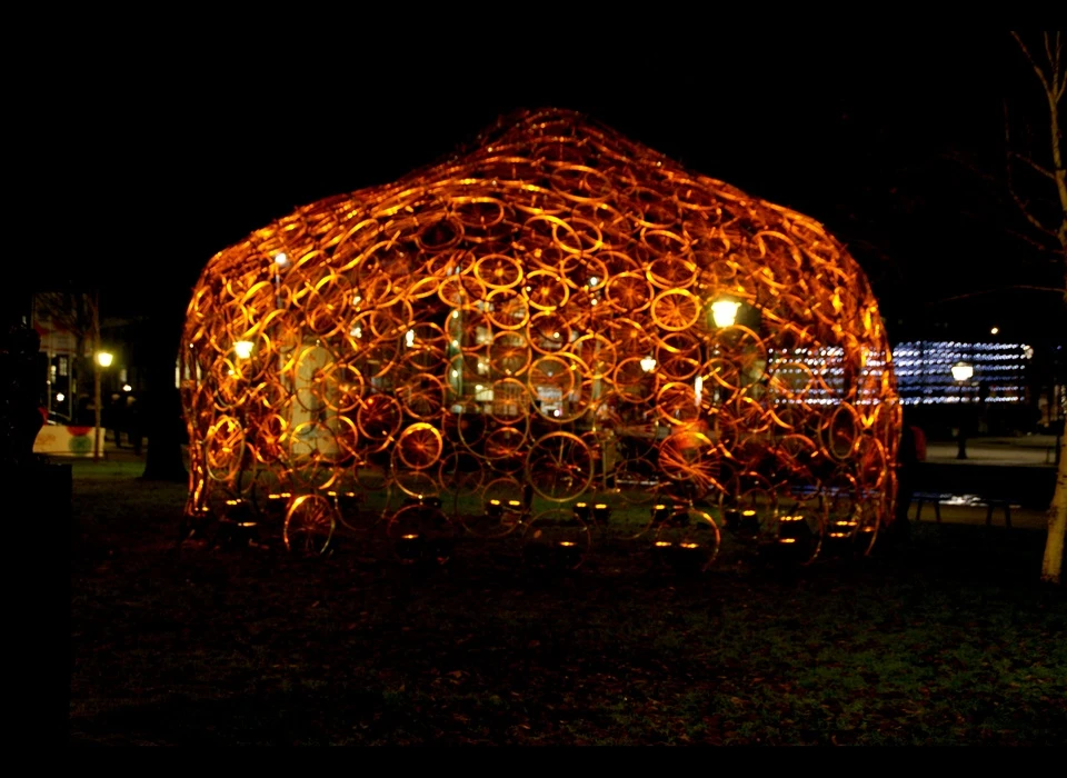 Wie deze koepel tot leven wil zien komen, zal de handen uit de mouwen moeten steken. 'Re(bi)cycle Dome' is opgebouwd uit 360 
					  fietsvelgen van afgedankte fietsen. Boven de koepel ‘zweeft’ een tweede laag van wielen, voorzien van lichtbronnen. Overdag dragen de wielen bij aan het kunstwerk , 's avonds verdwijnen ze in de duisternis 
					  en beschijnen ze de koepel, mits ze van energie worden voorzien. Bezoekers kunnen hiervoor een ouderwetse waterpomp bedienen. Een fietswiel is volgens Popov de ultieme Nederlandse gadget, volledig doordacht 
					  en een goede bouwsteen. (Vasili Popov (RU) studeerde aan het Moscow Architectural Institute is daarna zijn eigen studio in Amsterdam begonnen. Het verminderen van energieverbruik en het gebruik van 
					  duurzame materialen optimaliseren is belangrijk voor hem.) 2014