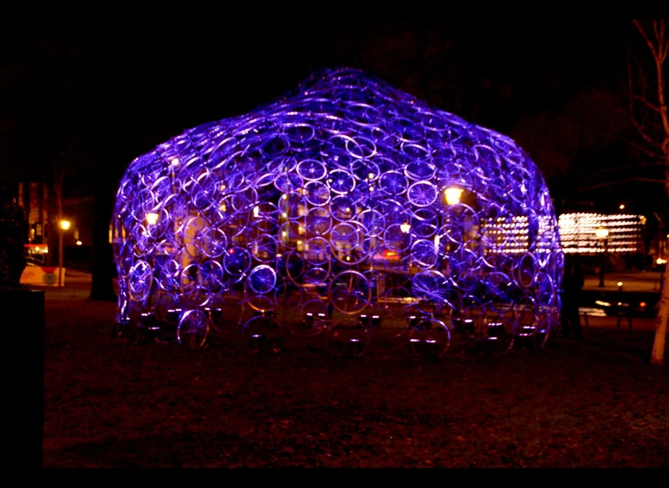 Wie deze koepel tot leven wil zien komen, zal de handen uit de mouwen moeten steken. 'Re(bi)cycle Dome' is opgebouwd uit 360 
					  fietsvelgen van afgedankte fietsen. Boven de koepel ‘zweeft’ een tweede laag van wielen, voorzien van lichtbronnen. Overdag dragen de wielen bij aan het kunstwerk , 's avonds verdwijnen ze in de duisternis 
					  en beschijnen ze de koepel, mits ze van energie worden voorzien. Bezoekers kunnen hiervoor een ouderwetse waterpomp bedienen. Een fietswiel is volgens Popov de ultieme Nederlandse gadget, volledig doordacht 
					  en een goede bouwsteen. (Vasili Popov (RU) studeerde aan het Moscow Architectural Institute is daarna zijn eigen studio in Amsterdam begonnen. Het verminderen van energieverbruik en het gebruik van 
					  duurzame materialen optimaliseren is belangrijk voor hem.) 2014