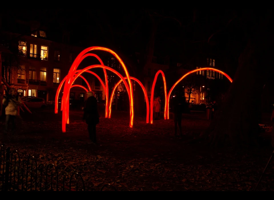 Het is alsof je een foto binnenloopt van iemand die met een rood licht bogen heeft getekend tegen de donkere lucht, zoals kinderen 
					  tijdens Oud en Nieuw hun naam schrijven met brandende sterretjes. De rode bogen bestaan uit plastic buizen, die van binnenuit worden verlicht met LED-lampjes. De simpele architectonische elementen voegen zich 
					  naar hun omgeving. ‘Constell.ation’ geeft je het gevoel dat je een fysieke ruimte betreedt wanneer je de bogen passeert. Een ruimte waarin alles anders lijkt dan erbuiten. (LIKEarchitects (PT) bestaat uit 
					  Diogo Aguiar, João Jesus en Teresa Otto. Ze richten zich met name op tijdelijke installaties. Met hun werk willen ze mensen de ruimte op een nieuwe manier laten ervaren.) 2014