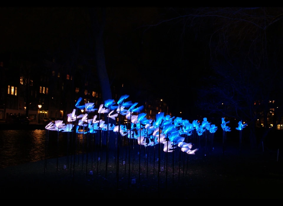 Een groep stralende vlinders, die met honderden tegelijk zweven in een vlucht opwaarts. ‘On the Wings of Freedom’ gaat over de indrukwekkende 
					  manier waarop technologie ons als samenleving verandert en hoe weinig we daarbij stilstaan. Tegelijkertijd gaat ‘On the Wings of Freedom’ over de transformatie van een stad. De vlinders zijn ook een advies van de 
					  kunstenaars: houd die verandering gaande, het is waar Amsterdam op draait. Men zegt dat één vlinderslag een storm kan veroorzaken. Laat al deze vlinders bij elkaar voor een orkaan van licht en creativiteit zorgen. 
					  (Aether & Hemera (IT) is een multidisciplinaire kunst- en designstudio, opgericht in 2008 door Gloria Ronchi en Claudio Benghi.) 2014