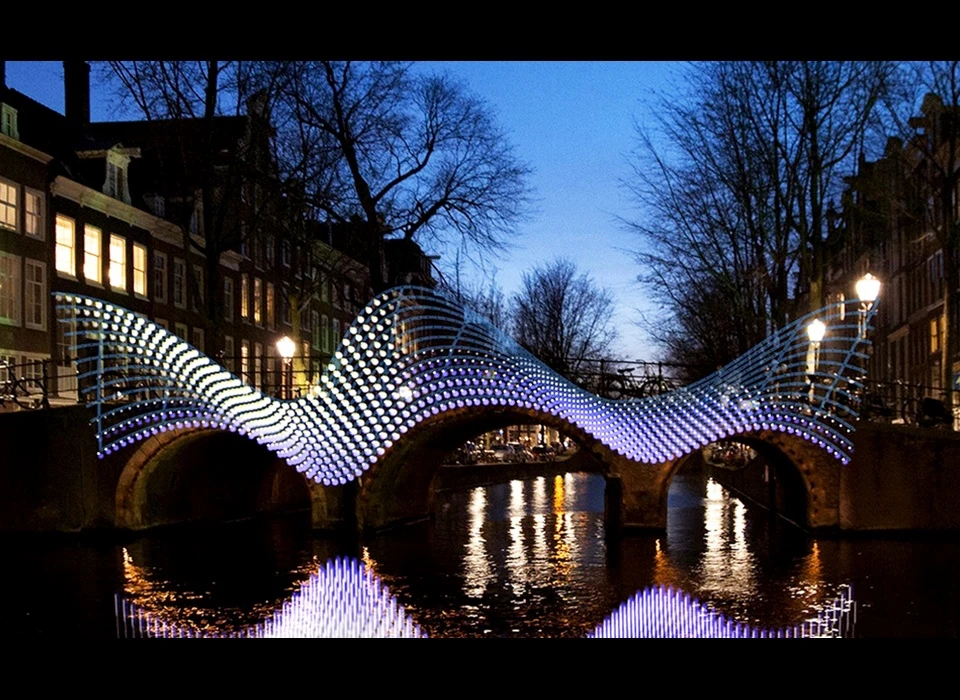 ‘Light Bridge’ is een ode aan de Amsterdamse brug maar verbindt ook diverse ideeën. Niet alleen dat van het straat- en waterleven, 
					  maar ook tussen de oude en de nieuwe architectuur van de stad. De lampjes zijn een knipoog naar de meest herkenbare lichtbron van de stad is: de bogen van lichtjes die aan de Amsterdamse bruggen zijn vastgemaakt. 
					  Ze reageren op beweging, zowel vanaf de straat als vanaf het water. (Frank Tjepkema (NL) studeerde aan de Design Academie in Eindhoven. Hij begon zijn ontwerpstudio Tjep. in 2001. Zijn werk is opgenomen in 
					  verschillende museum collecties.) 2014