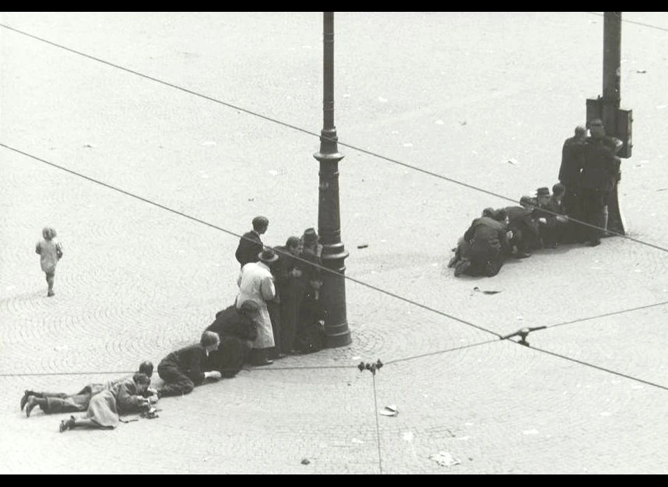 Dam 7 mei 1945 dekking zoeken op het plein voor de schietpartij door Duitse soldaten vanuit De Groote Club op de hoek van Paleisstraat en Kalverstraat