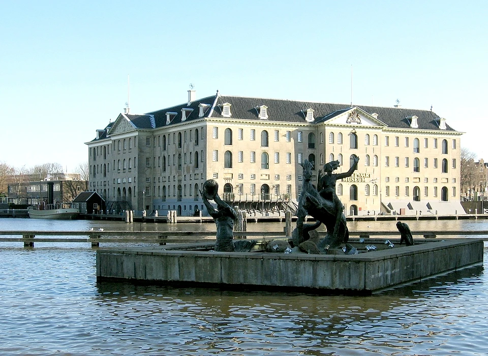 Scheepvaartmuseum vanaf Prins Hendrikkade op voorgrond beeldgroep afkomstig van de Surinamekade. De 
					  beeldengroep is een ontwerp van Albert Termote. De groep stelt Amphititre, echtgenote van Poseidon en godin van de zee, op een zeepaard voor. Haar zoon Triton blaast op een kinkhoorn om de golven te bedaren. Aangeboden bij 
					  het ..-jarig bestaan van de KNSM door het personeel. (circa.2000)