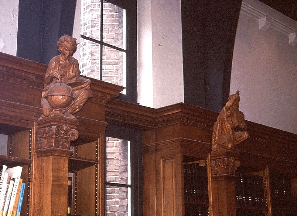 Mauritskade 63 Tropeninstituut houtsnijwerk door J.L.Vreugde op consoles boekenkast in leeszaal, links aardrijkskunde rechts Zending, een Petrusfiguur met een opengeslagen boek op Mattheus 28 vers 19. (1991)