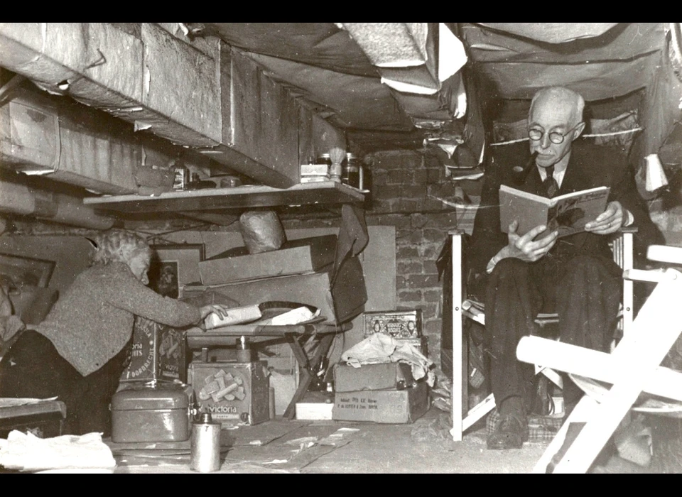 Nes 118 In de kelder van tabaksfabrikant Entcomayer demonstreert het echtpaar Coen en Ella van Eekenes-Jünge de ruimte voor bij hen aanwezige onderduikers. (1945)